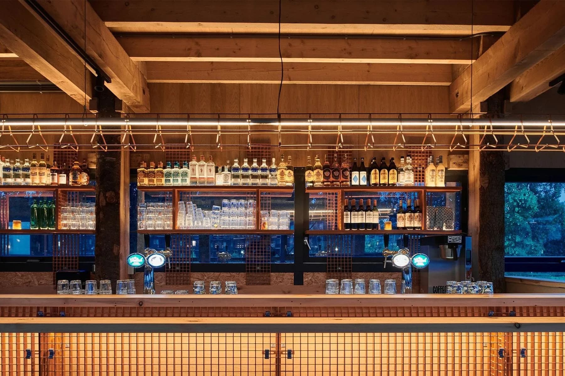 Bar met houten plafondbalken, flessenrek, tapkranen en een barfront van goudkleurige tegels