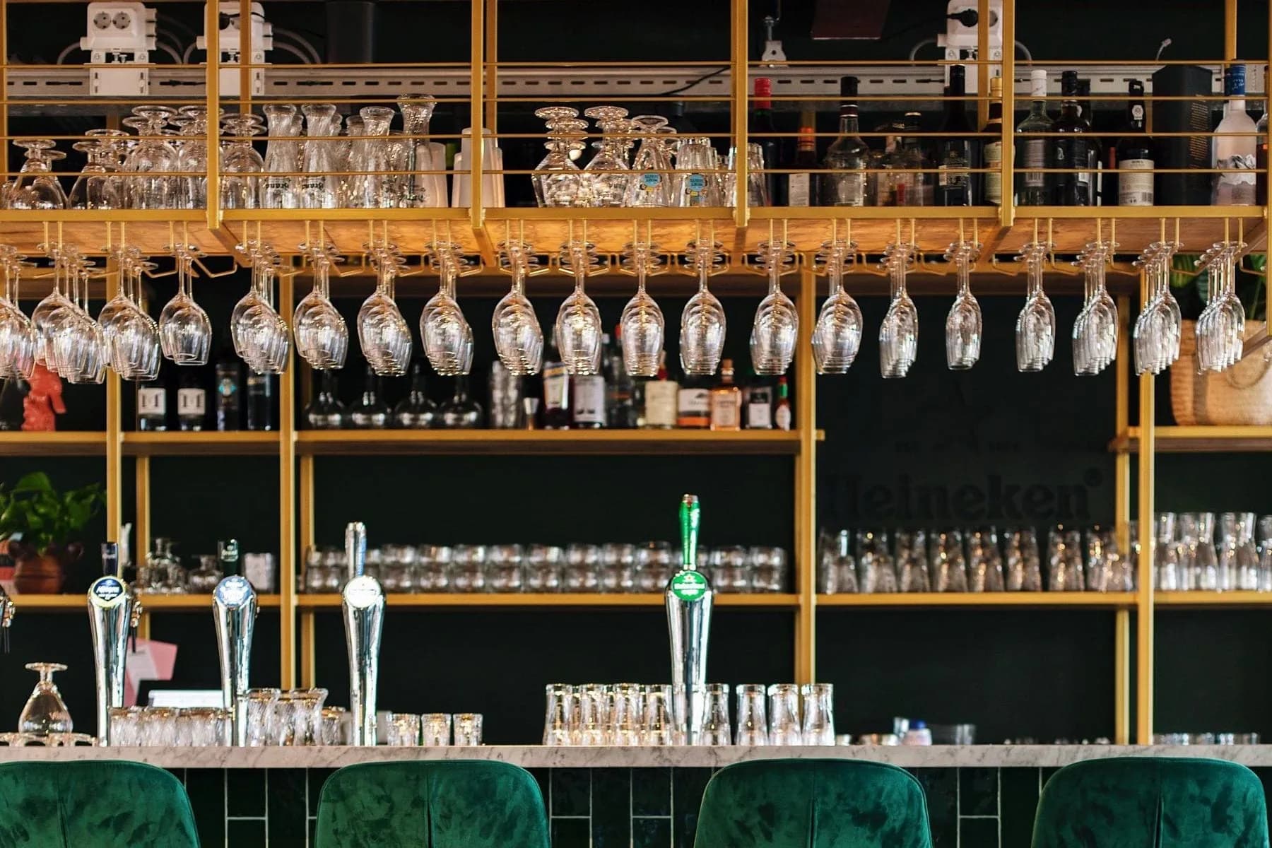 Groene barkrukken bij een bar met hangende glazen, tapkranen en groene tegels