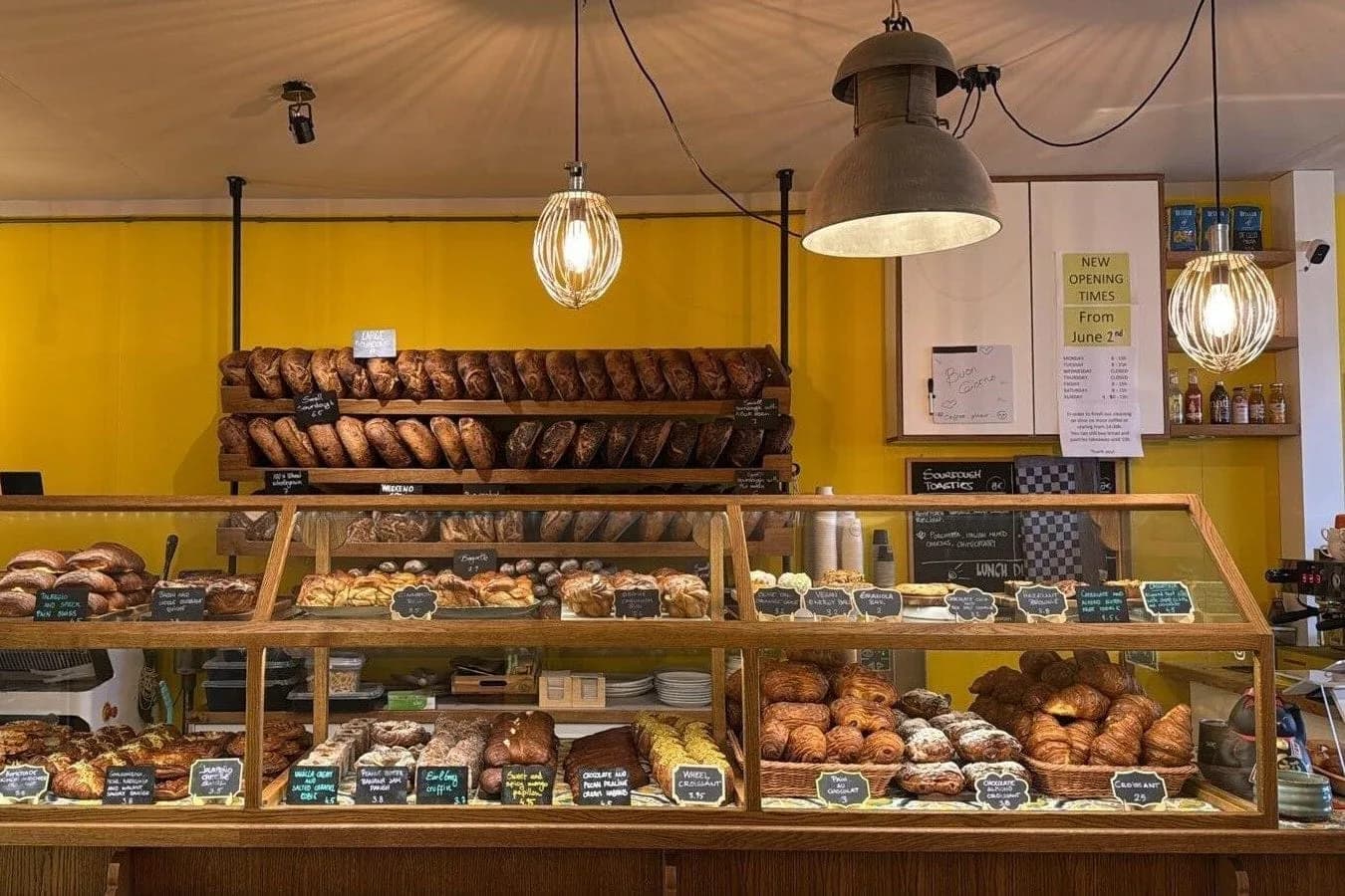 Bakkerijtoonbank met vitrines vol brood en gebak voor een gele muur met broodrekken