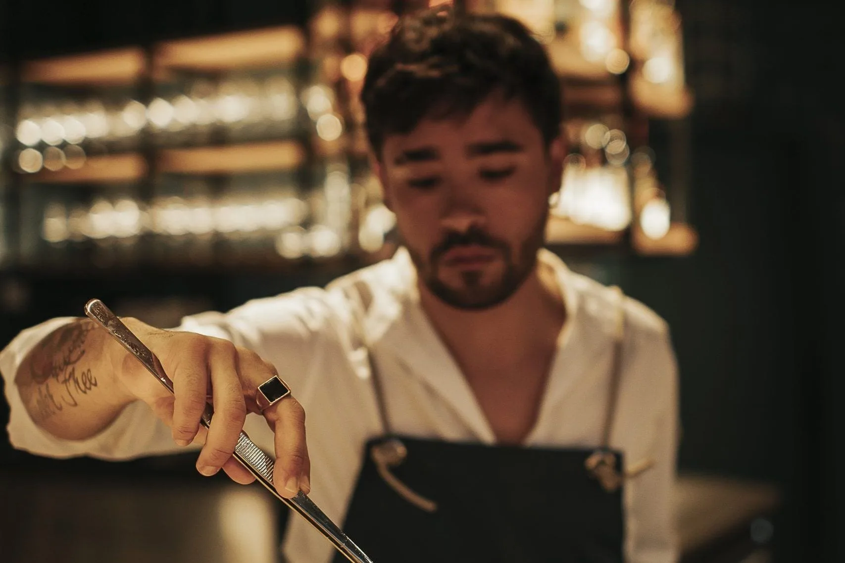 Bartender met schort raspt garnering boven drie cocktailglazen op de bar van Selva