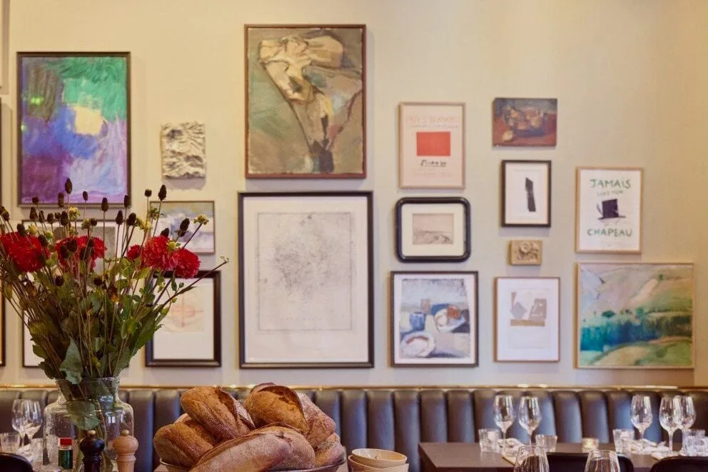 Broden op houten plank bij gedekte tafels, ingelijste kunstwerken aan de muur