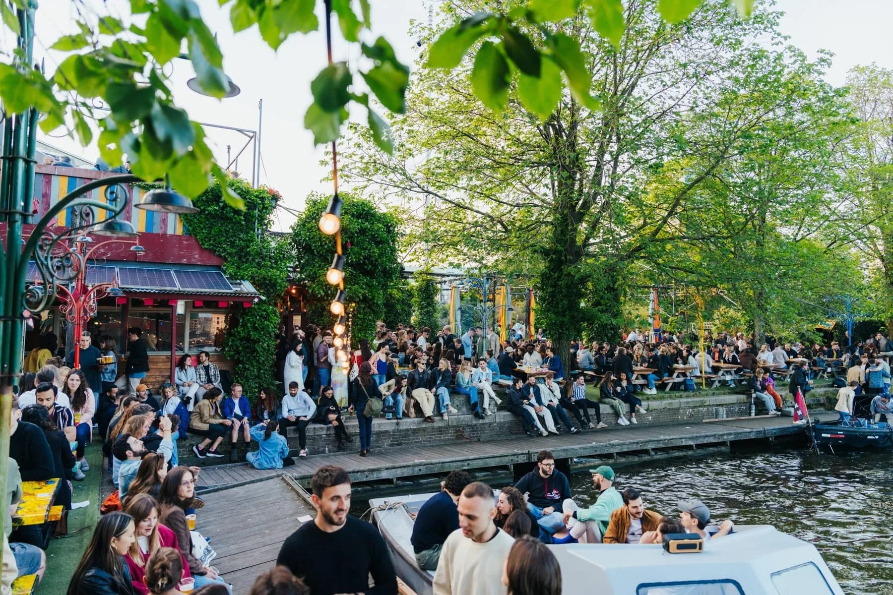 Drukke terras aan het water bij Hannekes Boom, met sloepen op het IJ