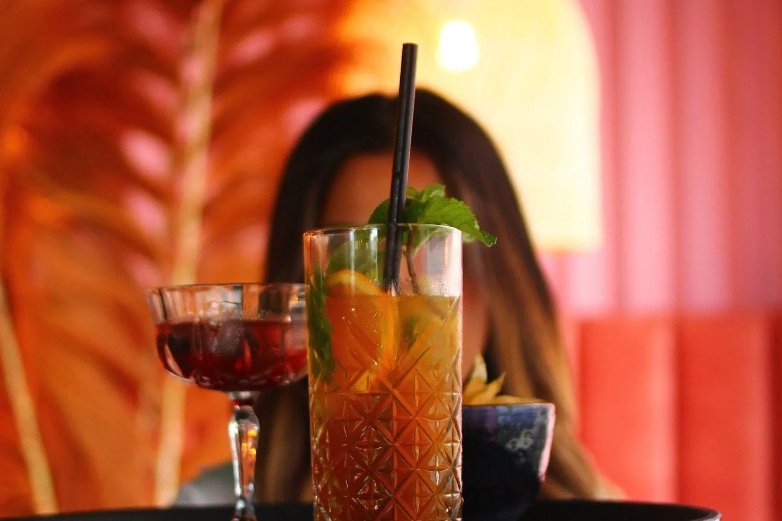 Medewerker houdt zwart dienblad met twee cocktails en een schaaltje voor zich uit