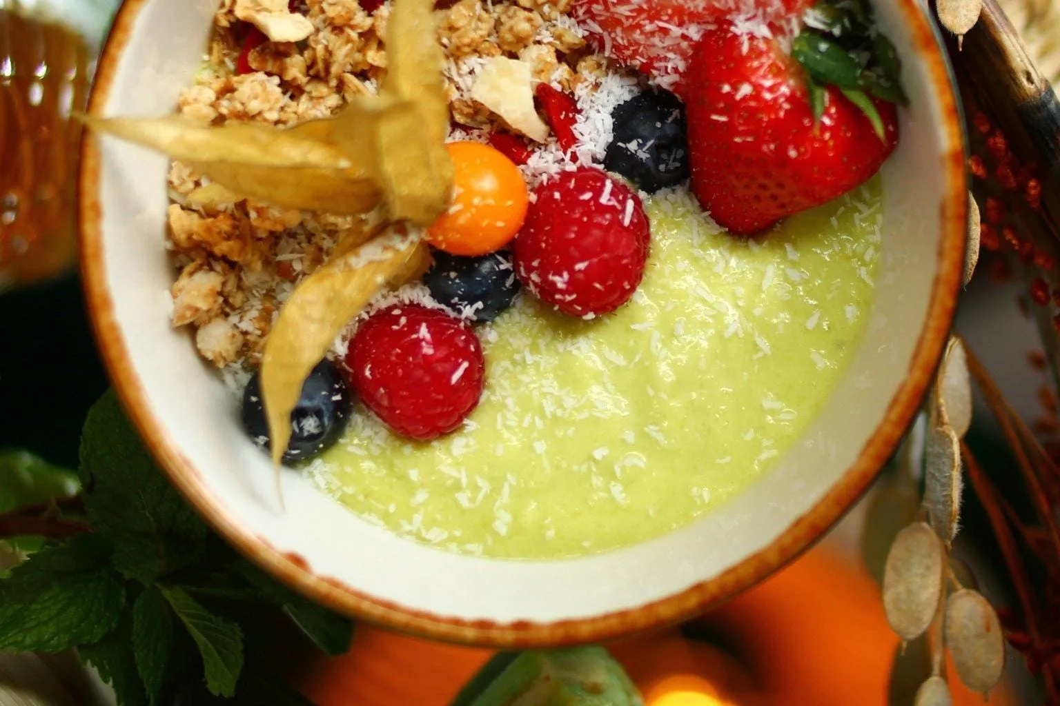 Kom met groene smoothiebowl, granola, aardbei, frambozen, bosbessen, kokosrasp en physalis op tafel