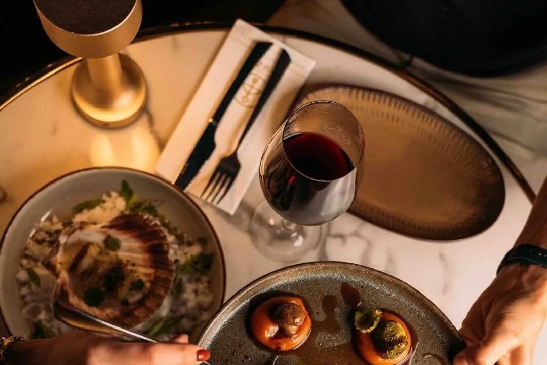 Bovenaanzicht van marmeren tafel met vleesgerecht, coquille, rode en witte wijn en handen