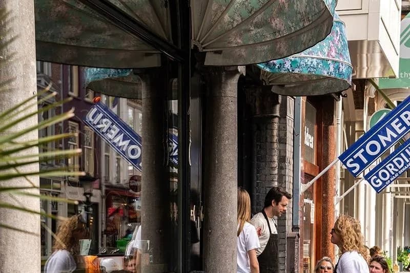 Vol terras met gasten in rieten stoelen, bediening met schort en parasols boven de gevel