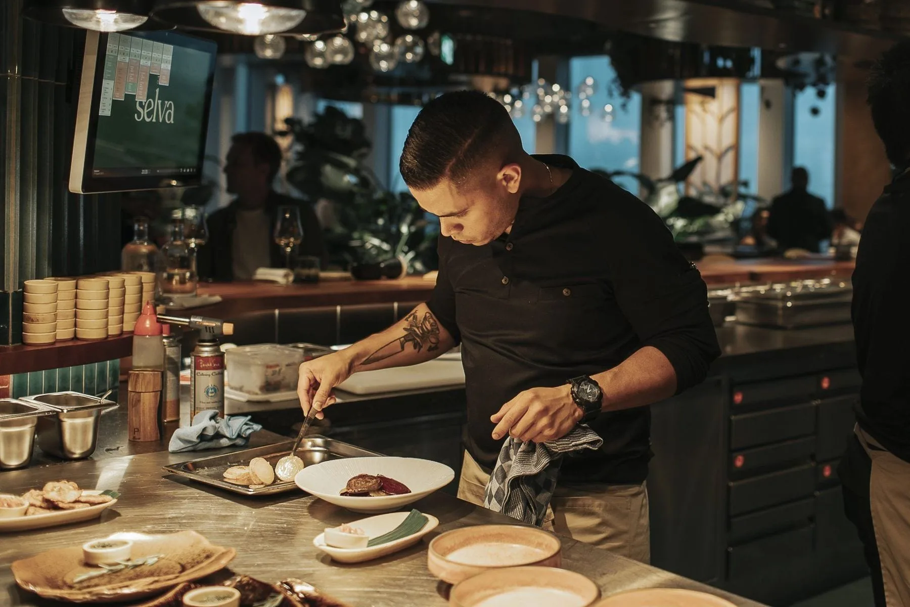 Kok in zwart shirt dresseert een gerecht aan de open keuken van het restaurant