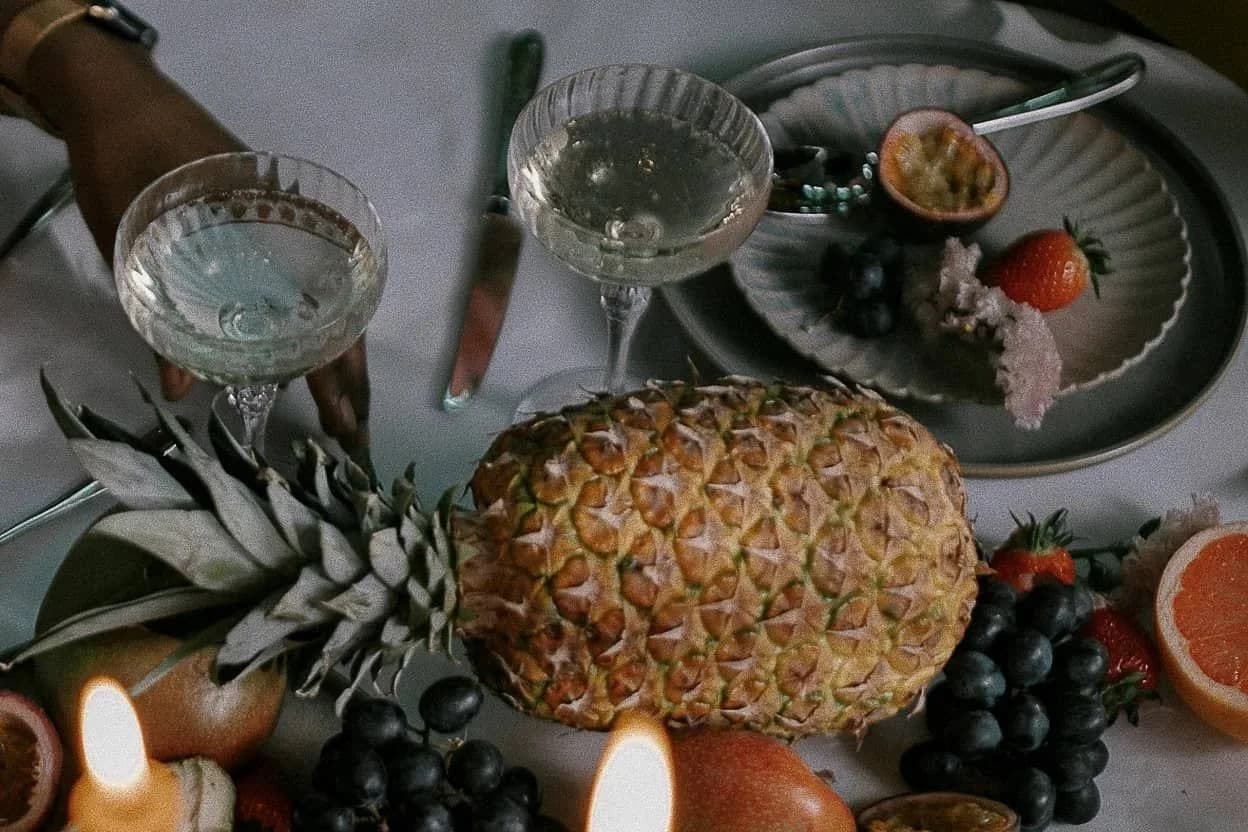 Gedekte tafel met ananas, grapefruit, druiven, aardbeien, coupeglazen en brandende kaarsen