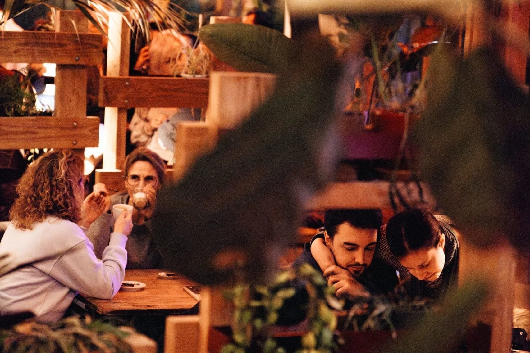 Gasten aan houten tafels tussen hangplanten, houten schotten en een discobal aan het plafond