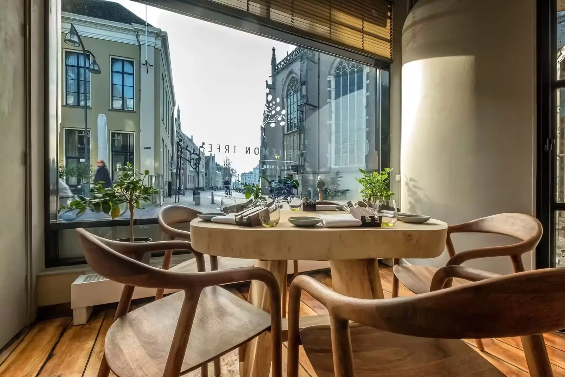Houten tafel met vier stoelen bij een raam met uitzicht op straat en kerk