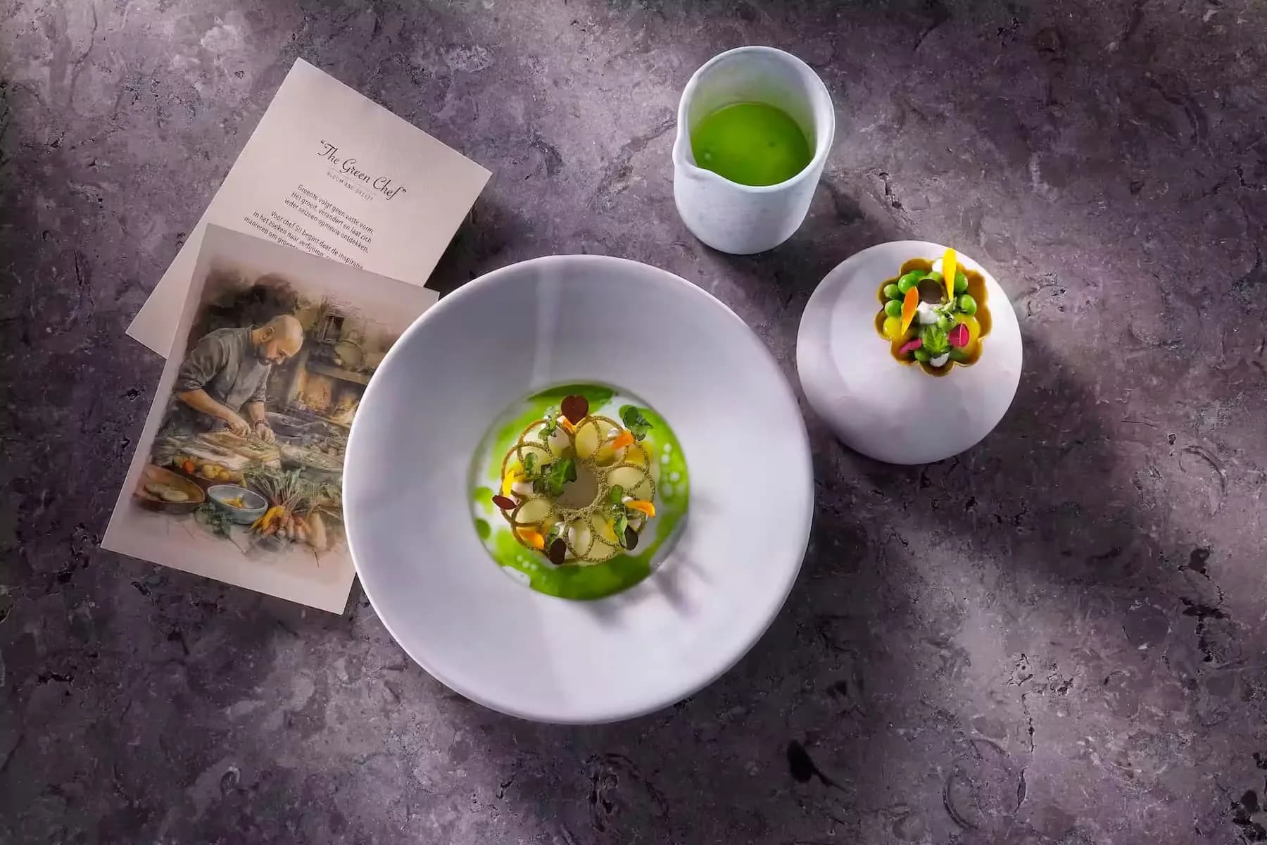 Diep bord met groene saus en groenten, kannetje, kommetje en twee kaarten op steen