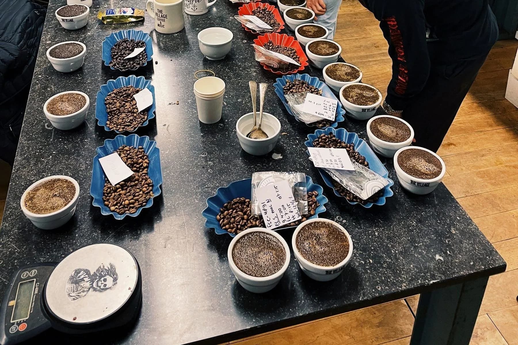 Twee personen ruiken aan kommen koffie aan een cuppingtafel voor een wereldkaart