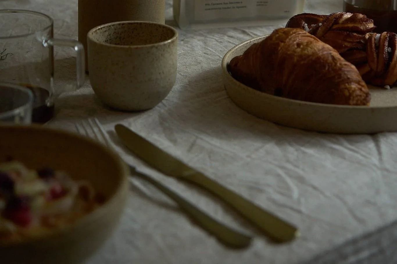 Hand pakt zak koffiebonen op tafel met croissants, keramieken beker, vaas en bestek