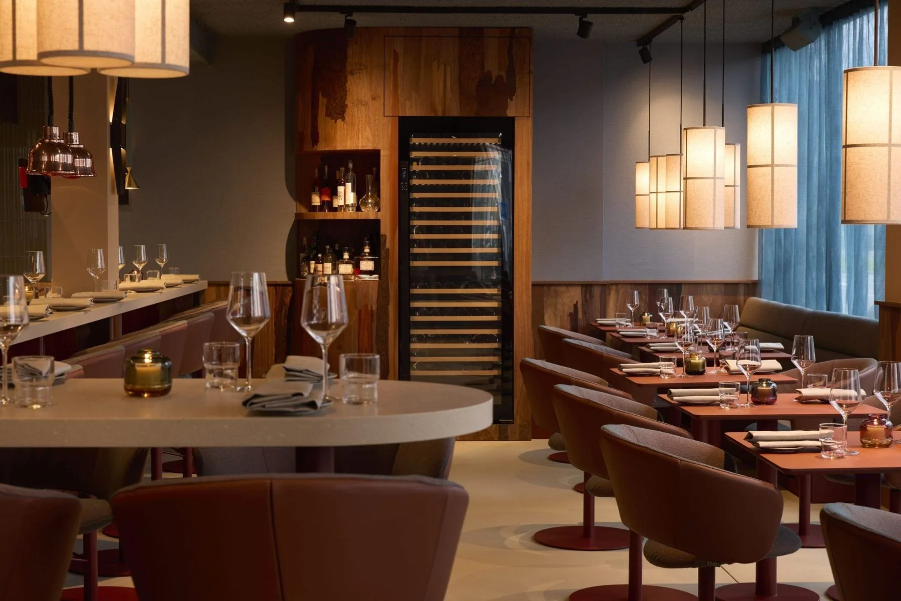 Restaurantzaal met gedekte tafels, hangende lampen, leren stoelen en een wijnklimaatkast tegen houten wand
